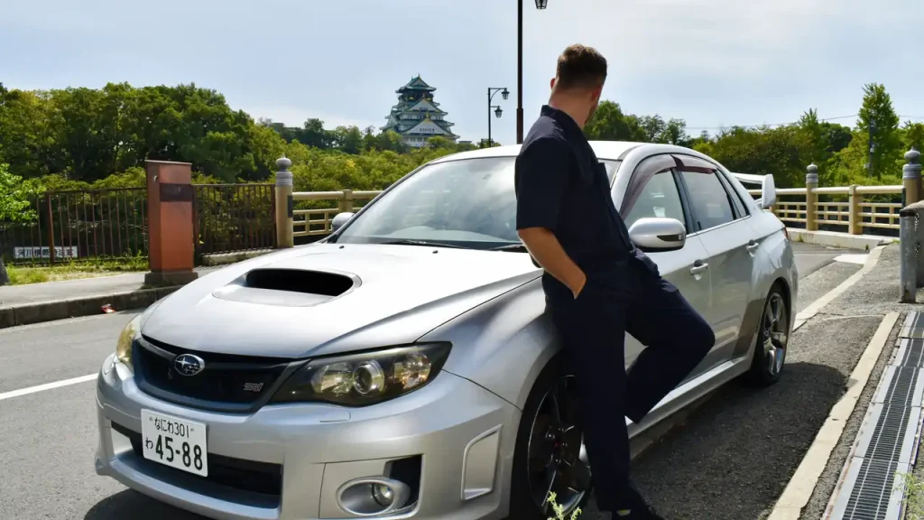 a man standing in front of a Subaru WRX in front of Osaka Castle